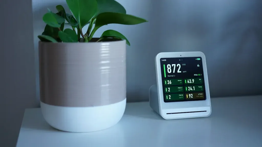 Digital indoor air monitor beside a potted plant