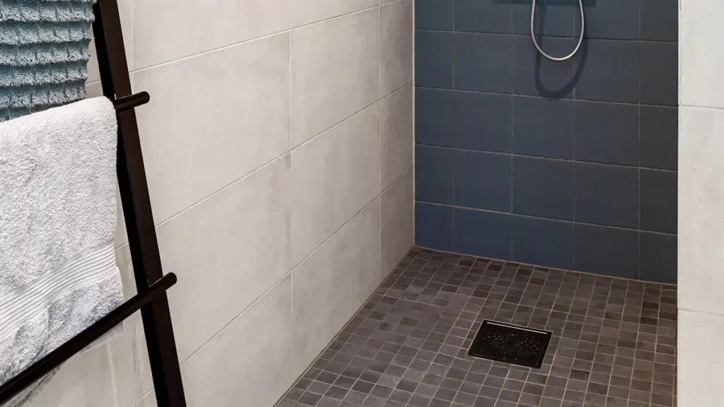 Walk in shower with mosaic floor tiles and a square drain