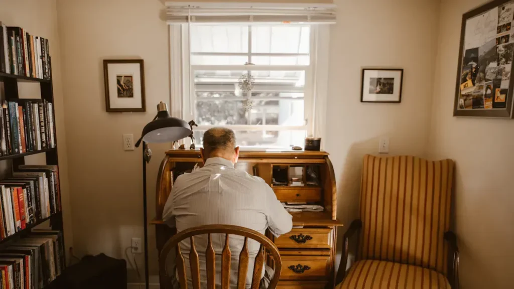 Person seated at a wooden desk beside a window