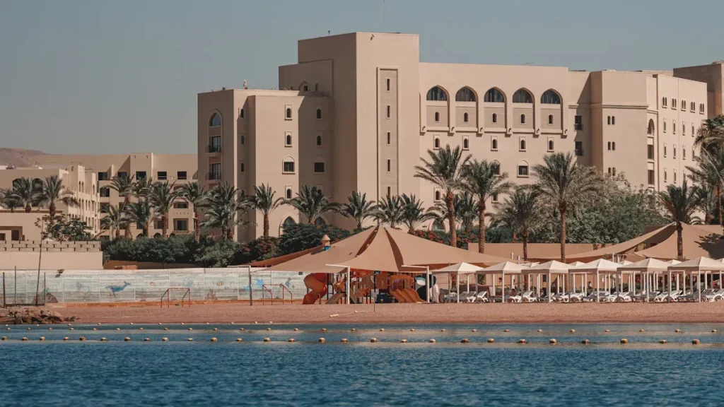 Waterfront resort buildings with palms and beach umbrellas